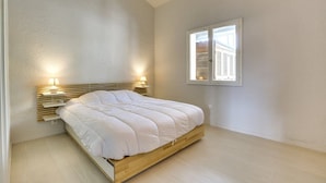 A bedroom with a bed, bedside lamps, a window, and a wooden headboard.