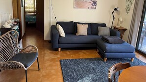 A living room with a dark blue sofa, a wicker chair, a wooden dining table, and a blue rug.
