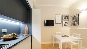 Et moderne køkken med indbygget ovn, vask og spiseområde med hvidt bord og stole.