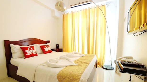 A hotel room with a bed, a bedside table with a phone, and a window with curtains. - ZEN Rooms Palanan (Makati)