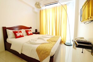 Habitación de hotel con cama, mesita de noche con teléfono y ventana con cortinas.