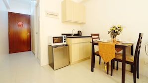 A compact kitchen with a microwave, a small refrigerator, and a sink. There is a dining table with chairs and a vase of flowers. - ZEN Rooms Palanan (Makati)