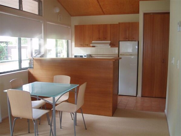 A compact kitchen with wooden cabinets, a white refrigerator, and a glass table with four chairs. - Boat Harbour Studio Apartments and Villas (Hervey Bay)