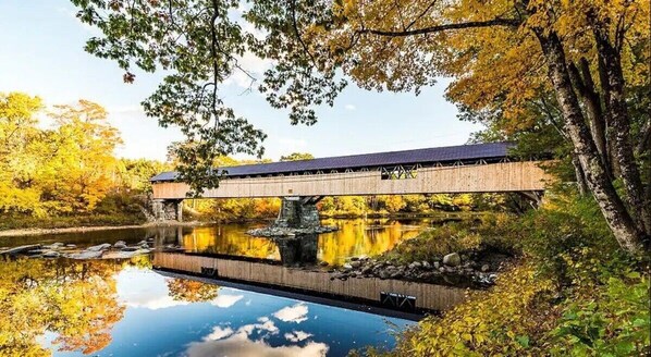 A wooden bridge over a calm river with autumn foliage.
