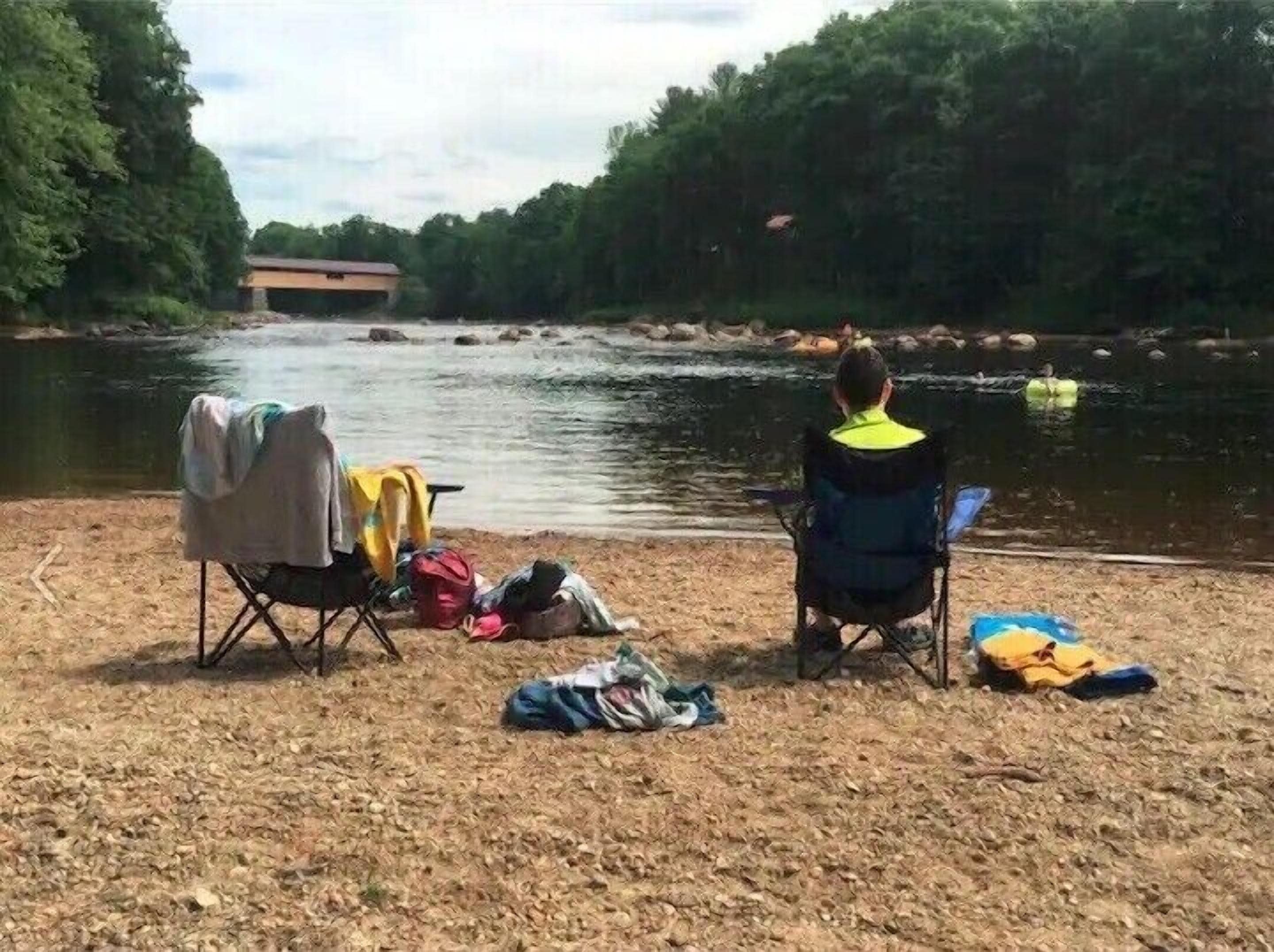 A campsite by a river with a covered chair and camping gear.