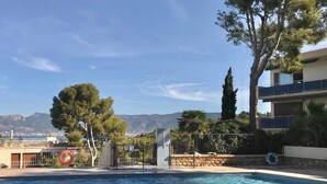 Une piscine avec vue sur les montagnes en arrière-plan, entourée d’arbres et bordée d’un bâtiment doté de balcons.