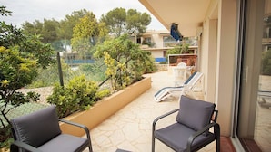 Un balcon avec deux chaises et une table, entouré de verdure et offrant une vue sur d’autres immeubles.