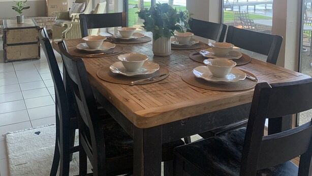 Zona pranzo con tavolo in legno apparecchiato per quattro persone, circondato da sedie. Ampia finestra con vista sull'esterno.