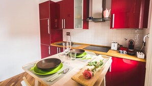A modern kitchen with red cabinets, a wooden dining table set for two, and a coffee machine on the counter. - GetTheKey San Felice Suite 1 (Bologna)