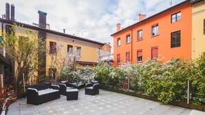 A courtyard with outdoor seating, surrounded by colorful buildings and flowering plants. - GetTheKey San Felice Suite 1 (Bologna)