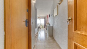 Un couloir avec des portes en bois, un sol carrelé et une vue sur une pièce où se trouvent un lit et un balcon.