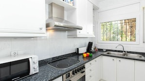 Een moderne keuken met witte kasten, een zwart aanrecht, een inbouwfornuis, een magnetron en een raam met uitzicht op groen.
