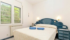 Een slaapkamer met een bed, twee nachtkastjes, een wandklok en een raam met jaloezieën.