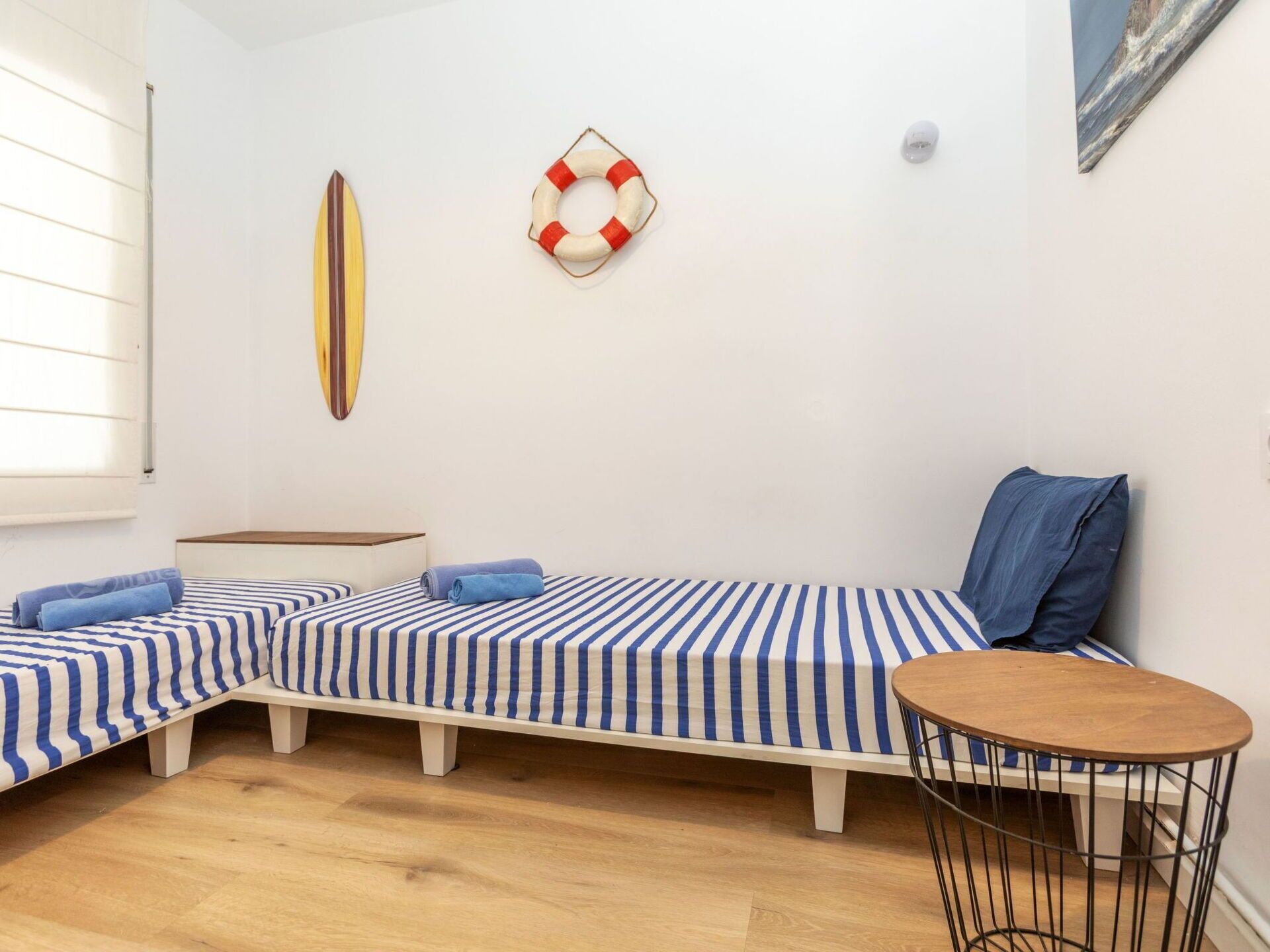 Une chambre avec deux lits simples, une petite table ronde et une planche de surf accrochée au mur.