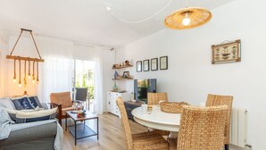A modern living room with a sofa, dining table, wicker chairs, and a TV.