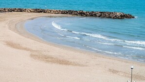 A sandy beach with a curved shoreline, a rocky breakwater, and a sailboat in the distance. - Lovely apartment for 6 guests with WIFI, pool, TV and balcony (Cunit)