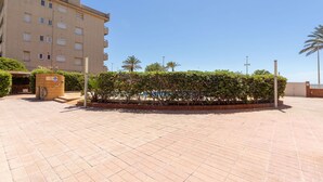 A building with multiple floors, a paved courtyard, and a small wooden structure with a sign. - Lovely apartment for 6 guests with WIFI, pool, TV and balcony (Cunit)