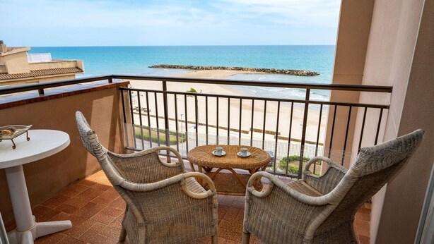 A balcony with wicker chairs and a small table, overlooking a beach and the sea. - Lovely apartment for 6 guests with WIFI, pool, TV and balcony (Cunit)