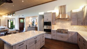 A modern kitchen with a large island, built-in ovens, and wooden cabinetry. - Spectacular luxury golf course view home in the heart of the Mauna Lani resort (Kamuela)