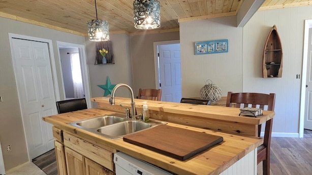 A kitchen with wooden countertops, a dishwasher, a sink, and pendant lights. - Drummond Island Hotel & Vacation Homes - Island Gem (Drummond)