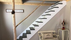 A staircase with a sign reading "THIS IS A HAPPY PLACE" and a bench with a cushion labeled "gather" near the bottom. - Drummond Island Hotel & Vacation Homes - Island Gem (Drummond)