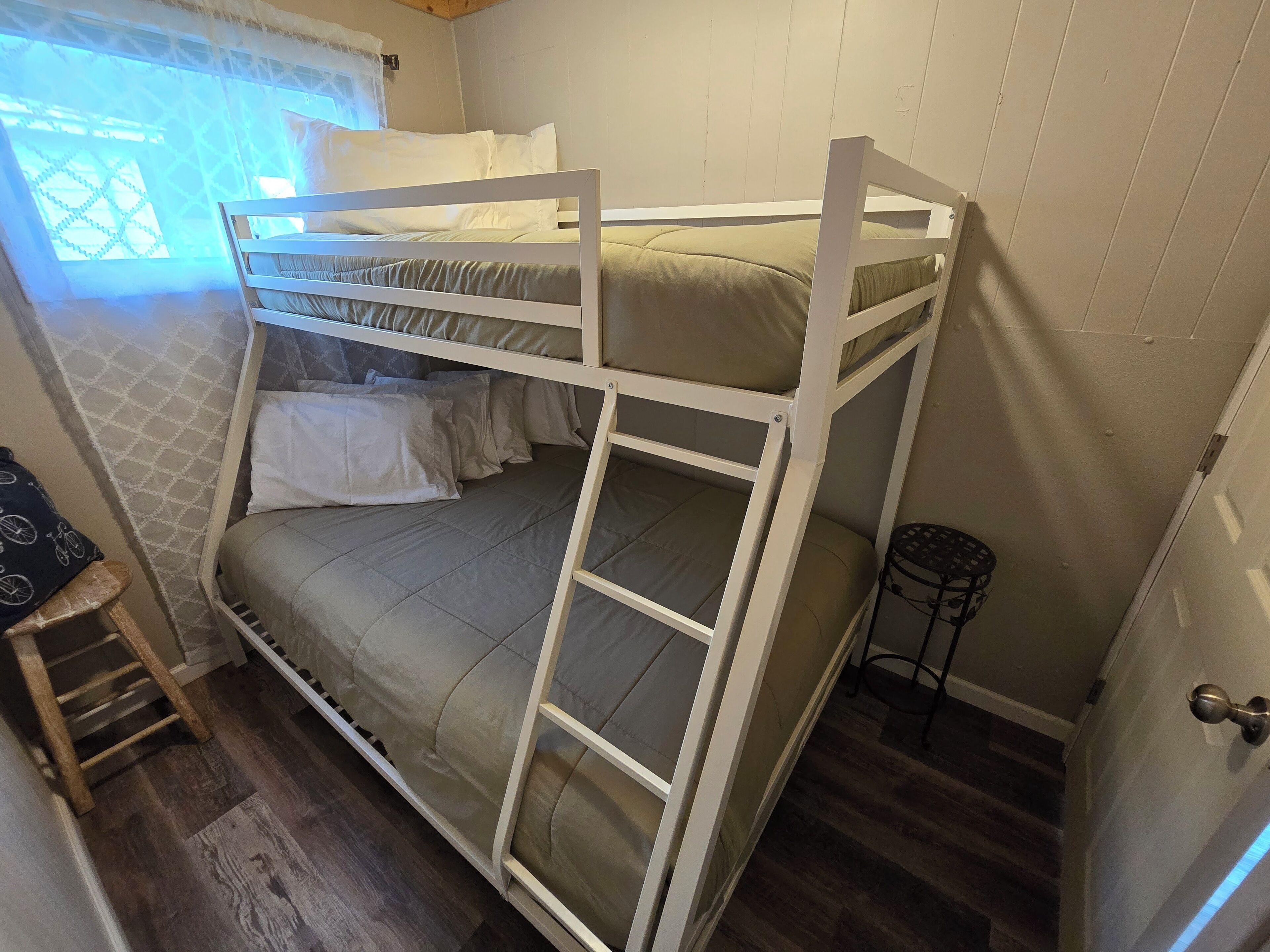 Een stapelbed met een ladder, een klein krukje en een deur met een hendel.