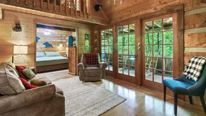 L’intérieur d’un chalet en bois, avec un canapé, un fauteuil et une vue sur l’extérieur grâce à de grandes fenêtres.
