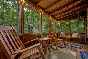Een houten vakantiehuisje met een veranda, houten meubels en lichtjes.