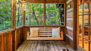 Une cabane en bois avec un banc-balançoire en bois, de grandes fenêtres et une vue sur une forêt.