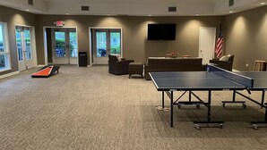 Um quarto com mesa de pingue-pongue, sofá e televisão na parede.