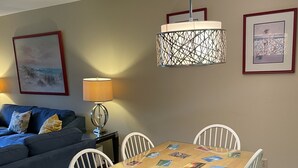 Uma área de refeições com uma mesa de madeira coberta de cartões postais, rodeada por cadeiras brancas.