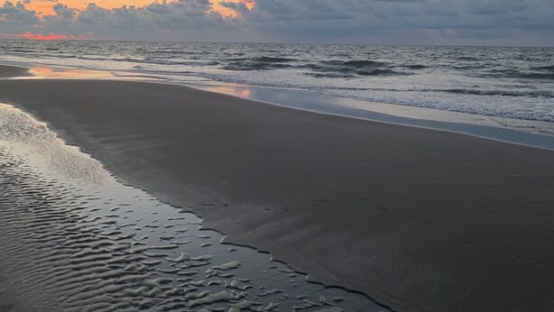 Uma praia com areia molhada e ondas suaves.