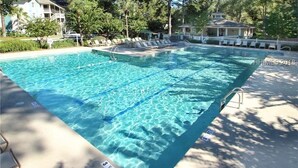 Uma piscina retangular com água azul cristalina, rodeada por espreguiçadeiras e um cercado branco.