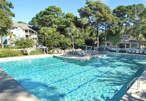 Une piscine rectangulaire à l’eau d’un bleu cristallin, entourée de chaises longues et d’une clôture blanche.