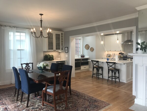 A spacious kitchen with a central island, wooden dining table with chairs, and a chandelier.
