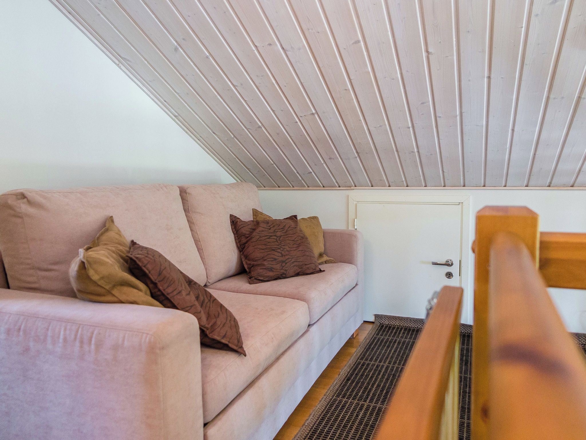 Una habitación con techo inclinado, un sofá con cojines, una puerta y un banco de madera.