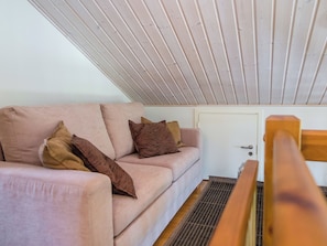 Um quarto com teto inclinado, um sofá com almofadas, uma porta e um banco de madeira.