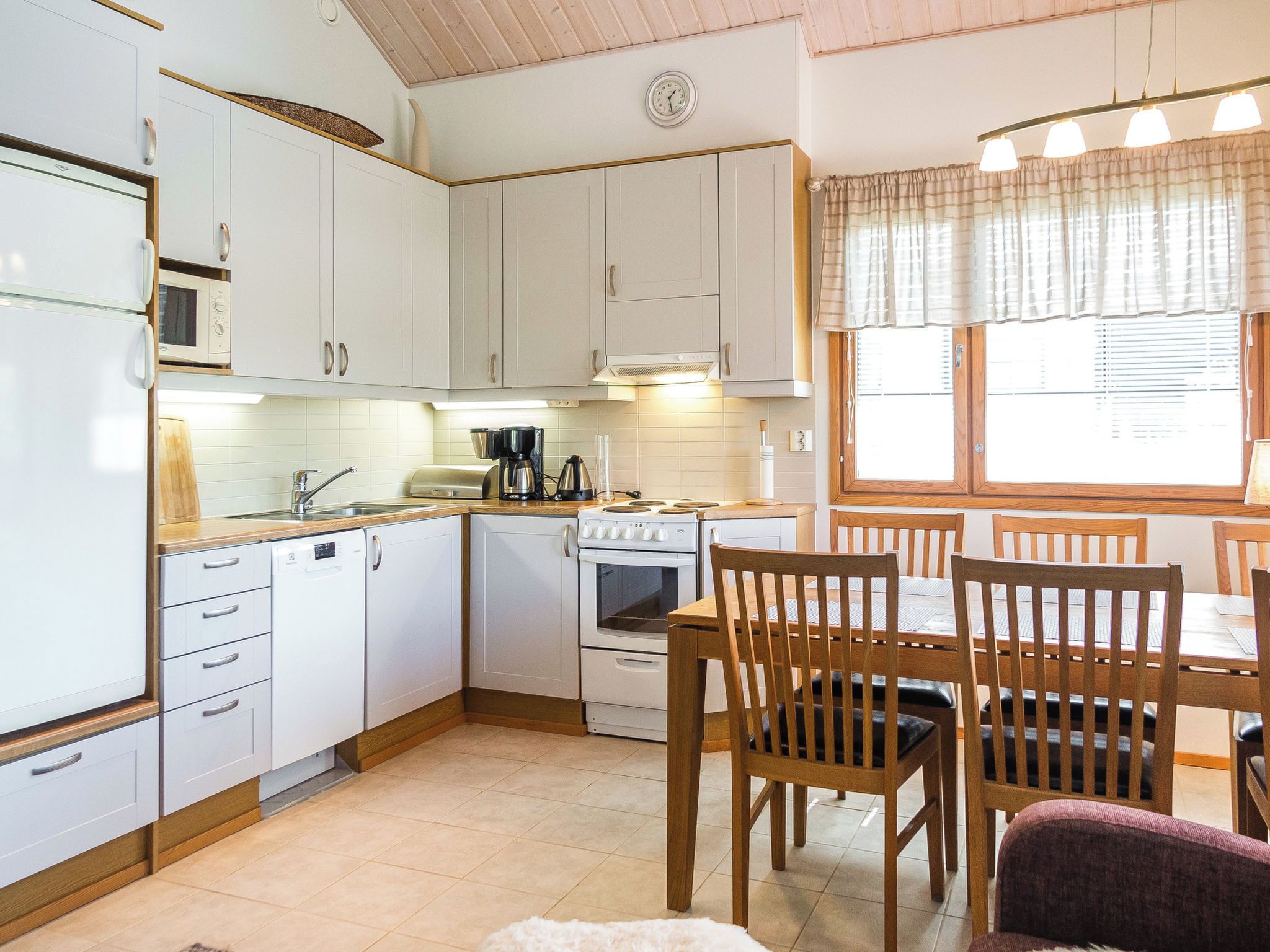 Une cuisine compacte avec des meubles blancs, une cuisinière, un four à micro-ondes et un coin repas comprenant des chaises et une table en bois.