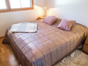 A bed with a quilted cover, two pillows, a bedside lamp, and a window with blinds. - Pike 2 as. 1 by Interhome (Nilsiä)