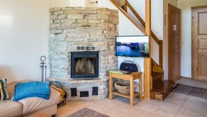 A cozy living room with a stone fireplace, a television mounted on the wall, and a wooden staircase. - Pike 2 as. 1 by Interhome (Nilsiä)