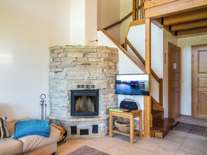 A living room with a stone fireplace, a television, and a wooden staircase. - Pike 2 as. 1 by Interhome (Nilsiä)