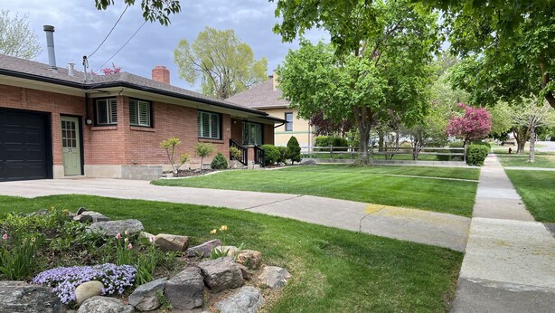A residential house with a brick facade, green shutters, and a well-maintained lawn with a rock garden and flowering plants. - Rustic Abode Entire Home- Near Logan (Hyde Park)