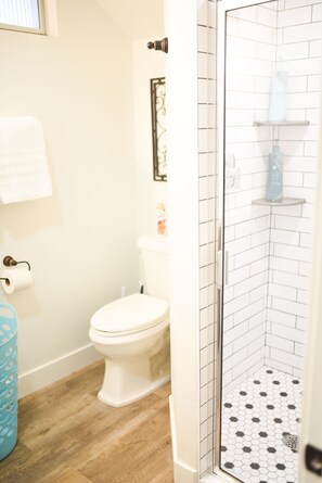 A bathroom with a toilet, a shower with white tiled walls, and a wooden floor.