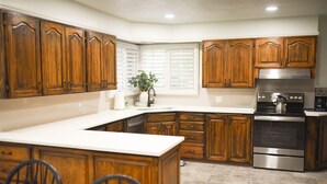 A kitchen with wooden cabinets, a stainless steel stove, and a window with blinds. - Rustic Abode Entire Home- Near Logan (Hyde Park)