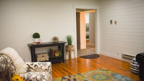 A living room with a patterned sofa, a console table with decorative items, a colorful rug, and wooden flooring. - Rustic Abode Entire Home- Near Logan (Hyde Park)