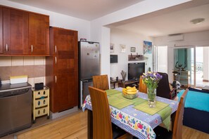 Una cocina compacta con armarios de madera, un refrigerador de acero inoxidable, un lavavajillas pequeño y una mesa de comedor con mantel floreado.