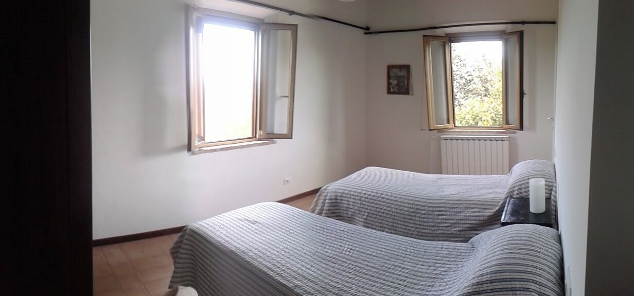 A room with two beds, two windows, a radiator, and a framed picture on the wall.