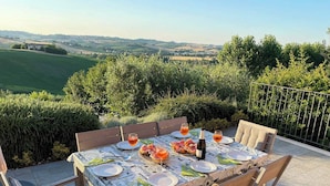 Une table de jardin, dressée avec des assiettes, des verres et une bouteille, entourée de chaises, et offrant une vue panoramique en arrière-plan.