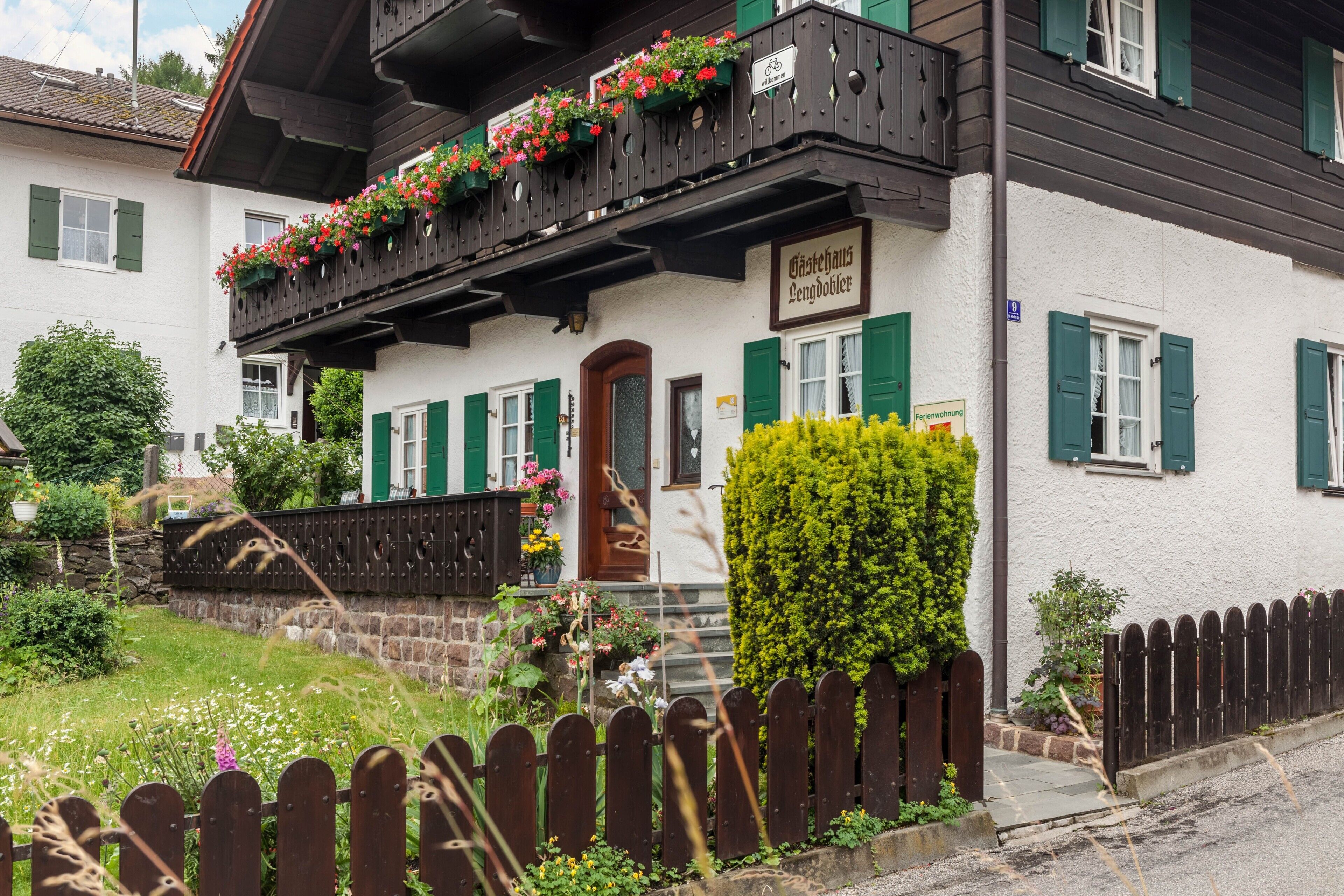 Un edificio tradicional con un balcón decorado con flores, un cartel que indica un restaurante y un jardín bien cuidado.