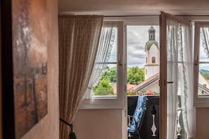 Une fenêtre ouverte donnant sur une église et un paysage verdoyant.
